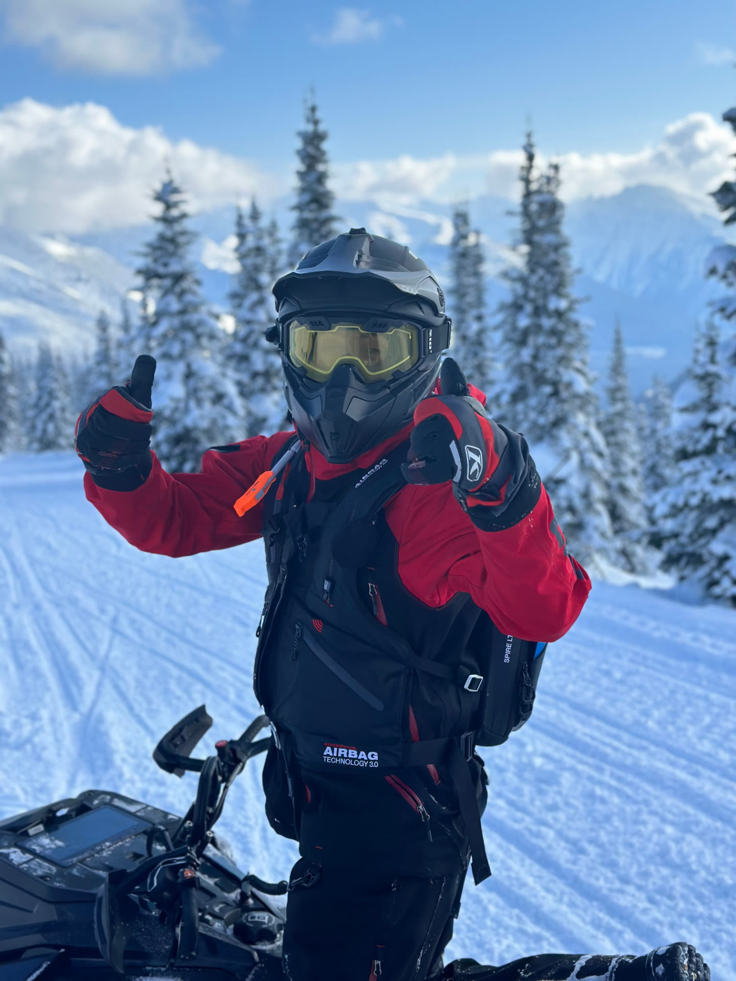 Mat giving two thumbs up on his snowmobile in the mountains